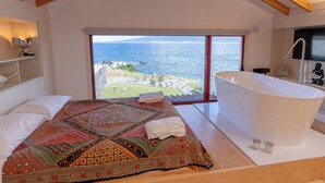 Een slaapkamer met een groot bed, uitzicht op zee en een moderne badkamer met een bad.