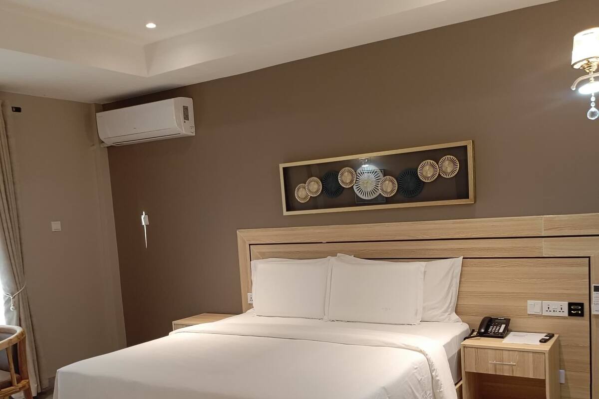 Une chambre d’hôtel moderne avec un grand lit, une table de chevet avec une lampe, un climatiseur fixé au mur et un élément décoratif mural.