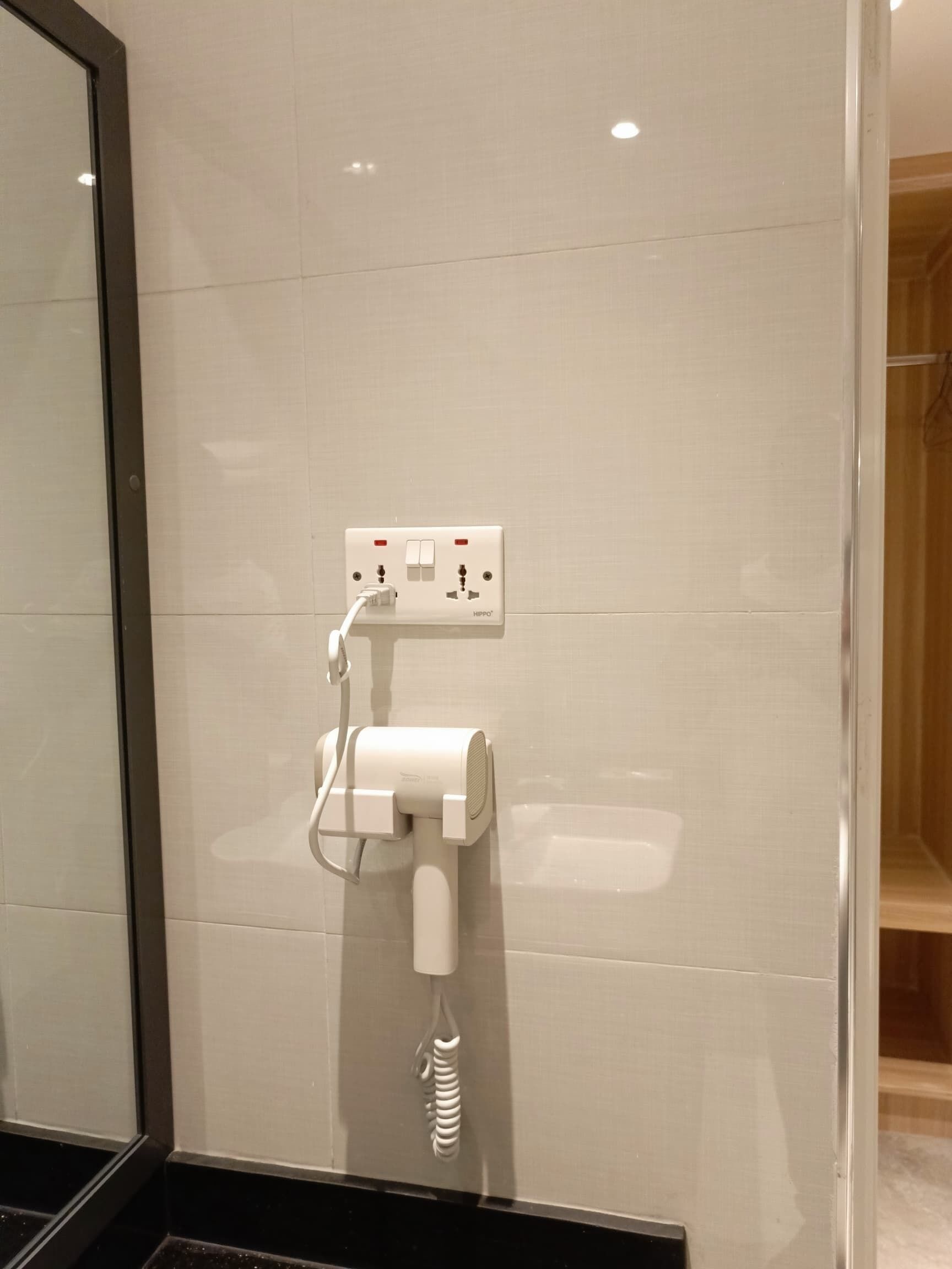 Een badkamer met een witte betegelde muur, een ingebouwde haardroger en een stopcontact met schakelaar.