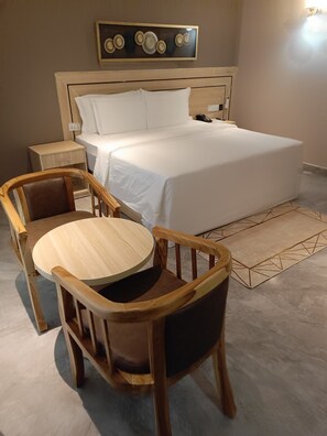 Um quarto com uma cama, uma mesa de cabeceira, uma cadeira e uma pequena mesa.