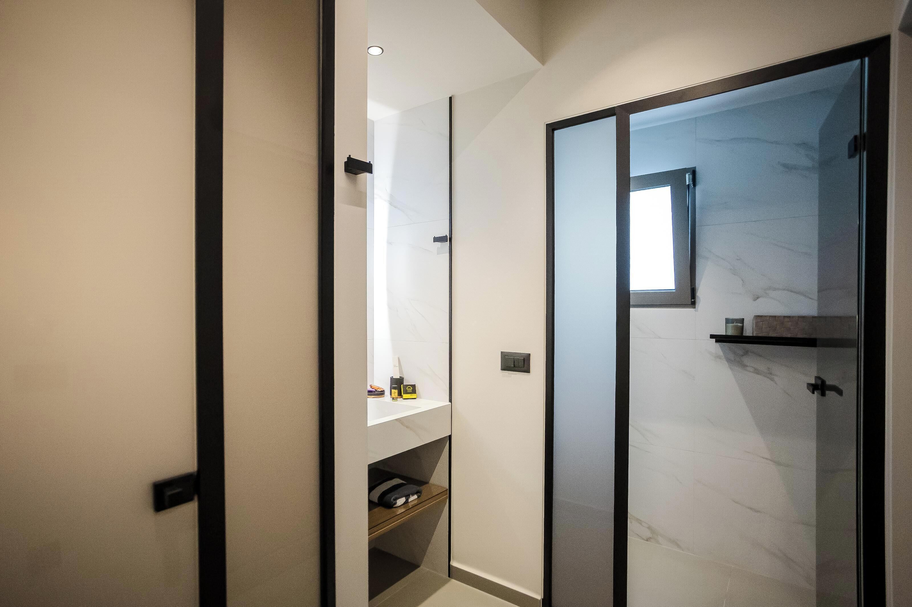 Een moderne badkamer met een glazen douchecabine, een ingebouwd kastje met toiletartikelen en een marmeren wand.