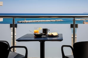 A balcony with a table set for breakfast, overlooking a rocky shoreline and the sea.