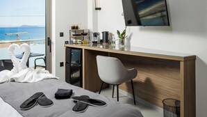 A modern hotel room with a bed, a desk, a chair, a TV, and a view of the sea. - Iria Sea View Room (Platanias)