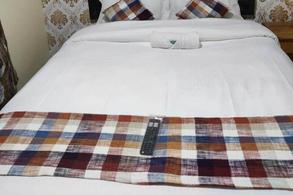 A neatly made bed with a plaid blanket, two pillows, and a remote control on the bed.
