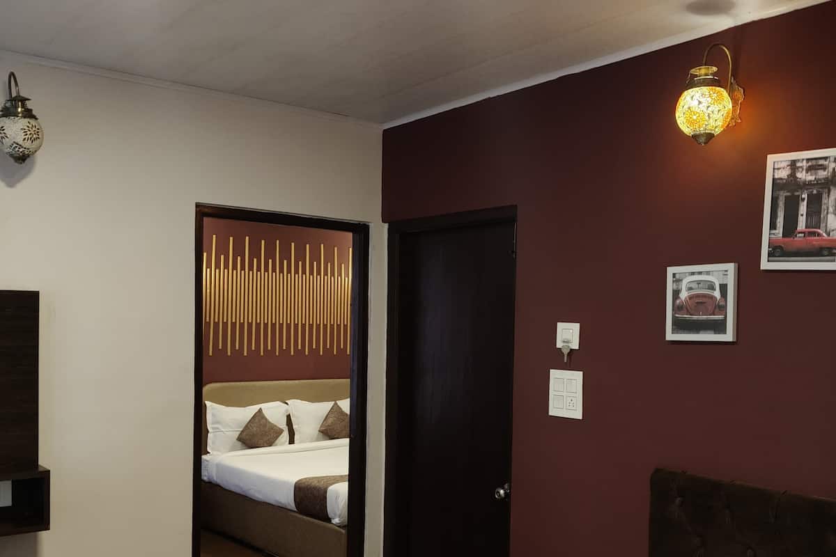 A hotel room with a bed, a small wooden nightstand, a wall-mounted light fixture, and a door leading to another room.
