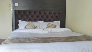 A bed with a dark headboard, white bedding, and striped pillows. - Hotel Route 55 (Darjeeling)
