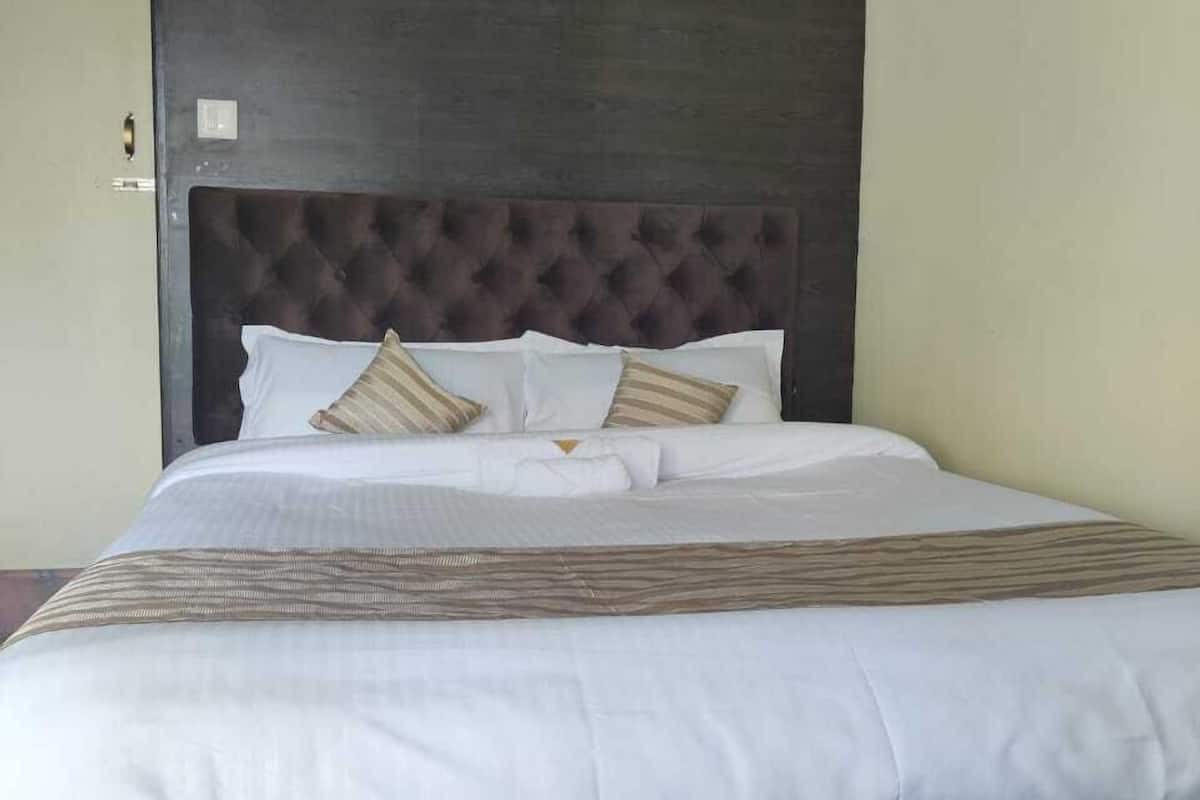 A bed with a dark headboard, white bedding, and striped pillows.