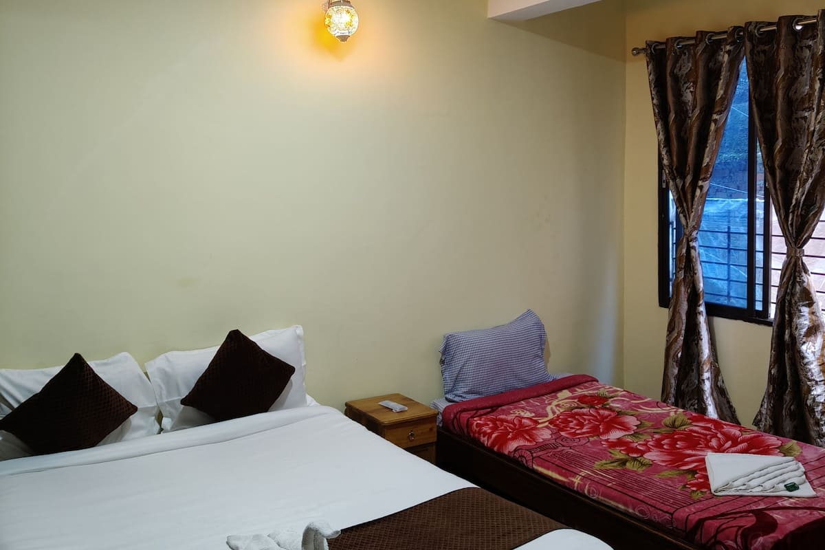 A hotel room with a large bed, a smaller bed, a nightstand, a wall-mounted light, and a window with curtains.