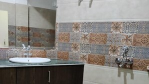 A bathroom with a tiled floor, a sink with a mirror, and a shower area. - Hotel Route 55 (Darjeeling)