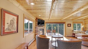 Una sala de estar acogedora con chimenea de piedra, vigas de madera en el techo y grandes ventanas que ofrecen vistas al exterior.