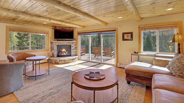 Una sala de estar acogedora con chimenea de piedra, vigas de madera en el techo y amplias ventanas que ofrecen vistas al exterior.