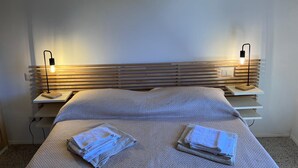 Una cama bien hecha con un edredón texturizado y dos toallas dobladas sobre la cama. Hay dos mesitas de noche con lámparas a cada lado de la cama.