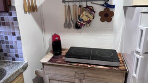 Una cocina con estufa, microondas y un refrigerador pequeño. Hay utensilios de madera colgados en la pared y una flor decorativa.