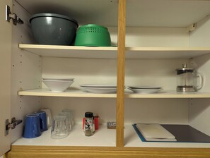 A kitchen with shelves holding bowls, plates, a coffee maker, and a spice rack.