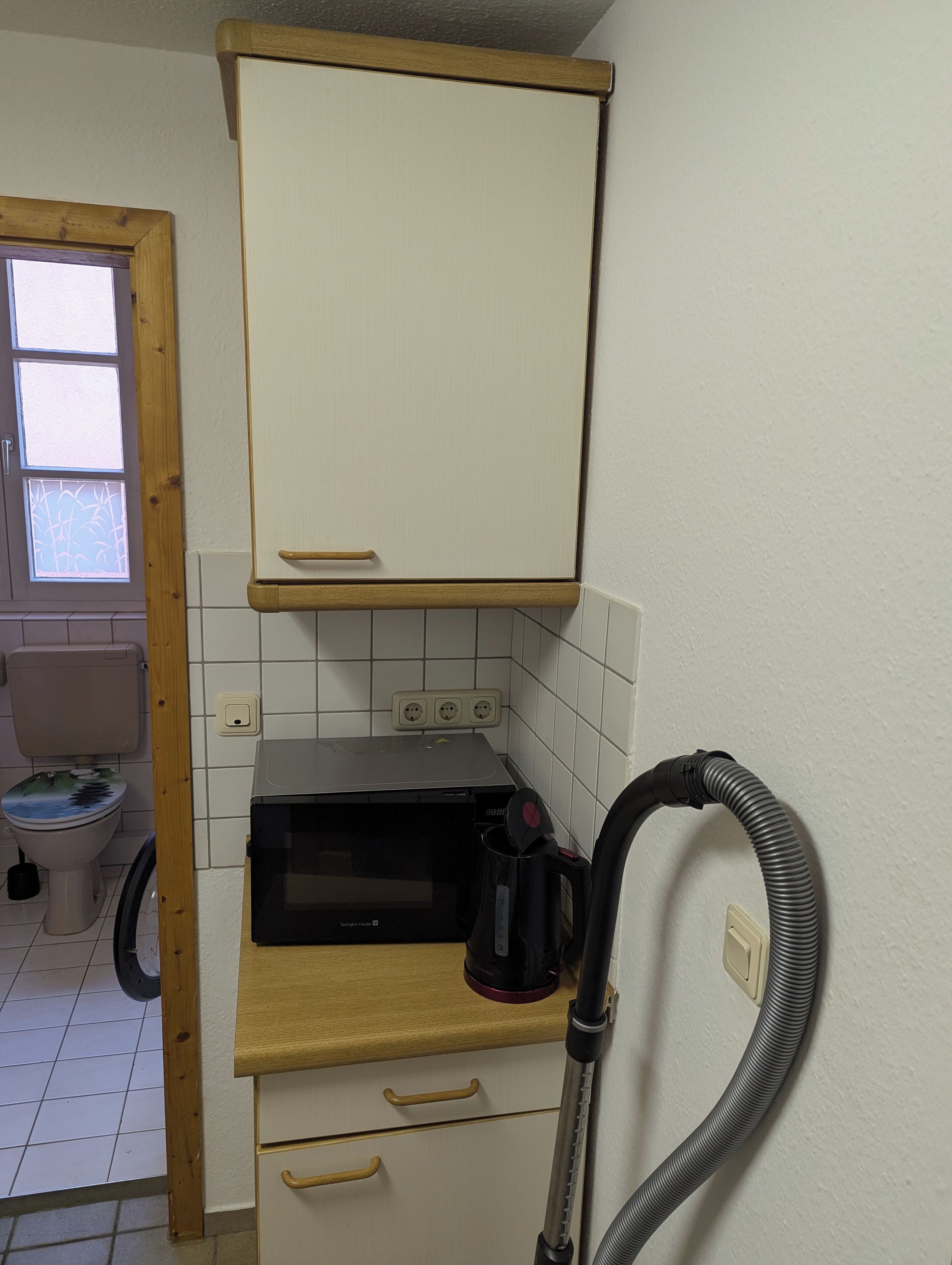Eine kompakte Küche mit Mikrowelle, Kaffeemaschine und Staubsauger.
