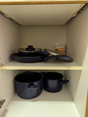 A kitchen with a white ceiling, a shelf with a frying pan and a box, and two pots on the lower shelf. - Accommodations in downtown Schwabach for 2 people (Schwabach)