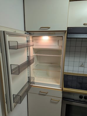 An open refrigerator with shelves and a freezer compartment, a kitchen counter with a stove, and a tiled backsplash. - Accommodations in downtown Schwabach for 2 people (Schwabach)