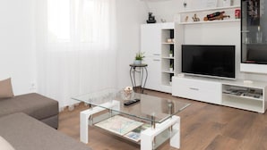 Un salon moderne avec une table basse en verre, un téléviseur à écran plat et un meuble de rangement blanc pour les appareils multimédias.