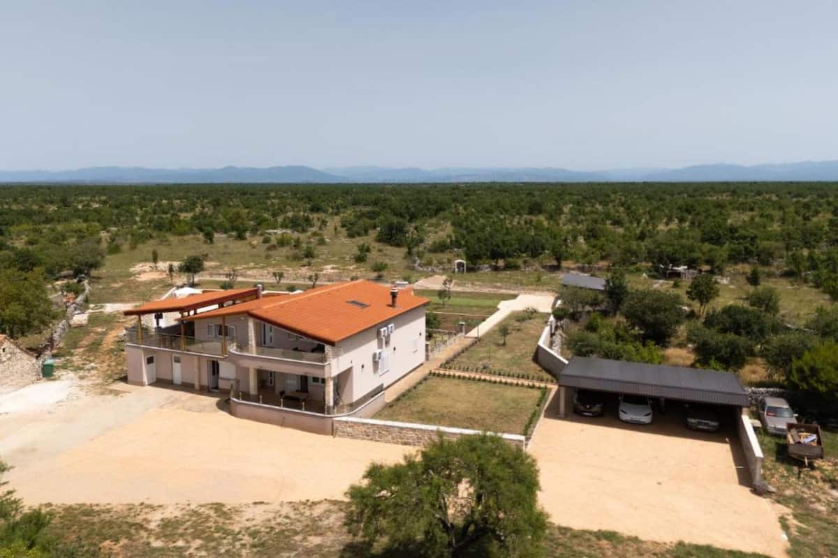 Une maison à deux étages avec un toit rouge, une terrasse couverte et une cour clôturée.