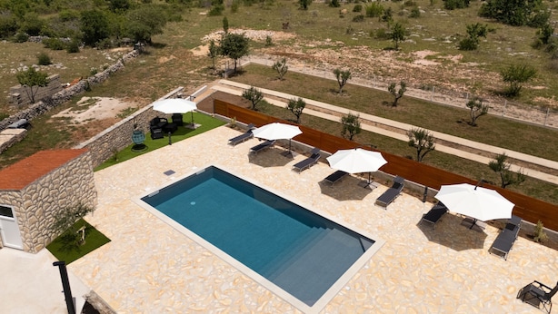 Un espace piscine agrémenté de chaises longues et de parasols, entouré d’un mur de pierre et offrant une vue sur un paysage naturel.