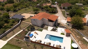 Vue aérienne d’une propriété résidentielle dotée d’une piscine, d’un patio couvert et d’une cour clôturée.