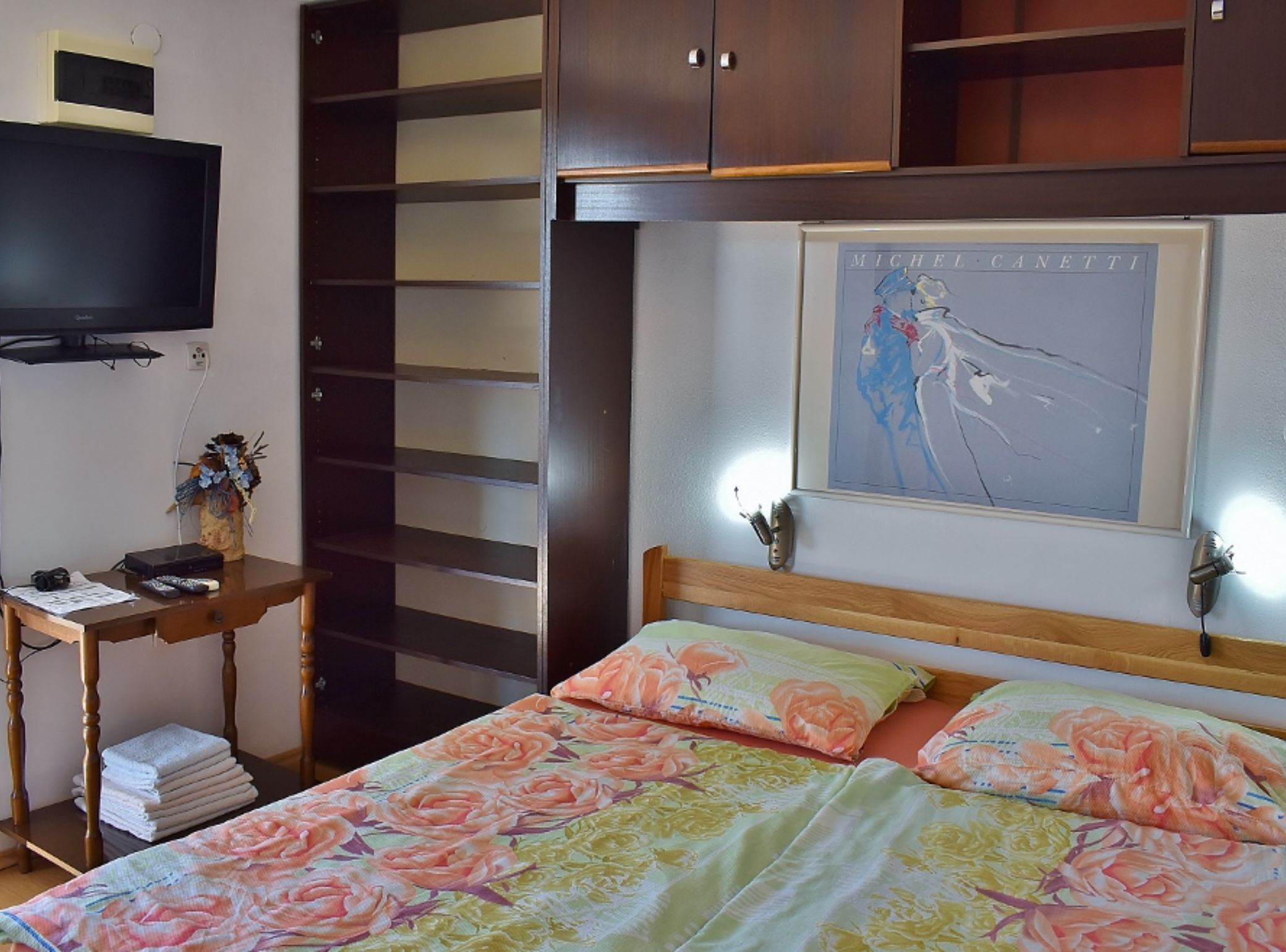 A bedroom with a bed, a desk, a television, and a framed picture on the wall.