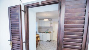 A kitchen with white cabinets, a tiled floor, and a dining area with a table and chairs. - Apartments Jug (Lopar)