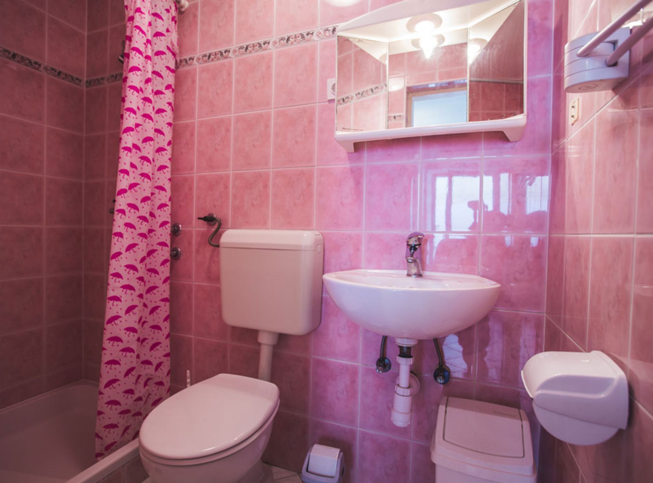 A bathroom with pink tiles, a toilet, a sink, and a shower curtain with a pattern.