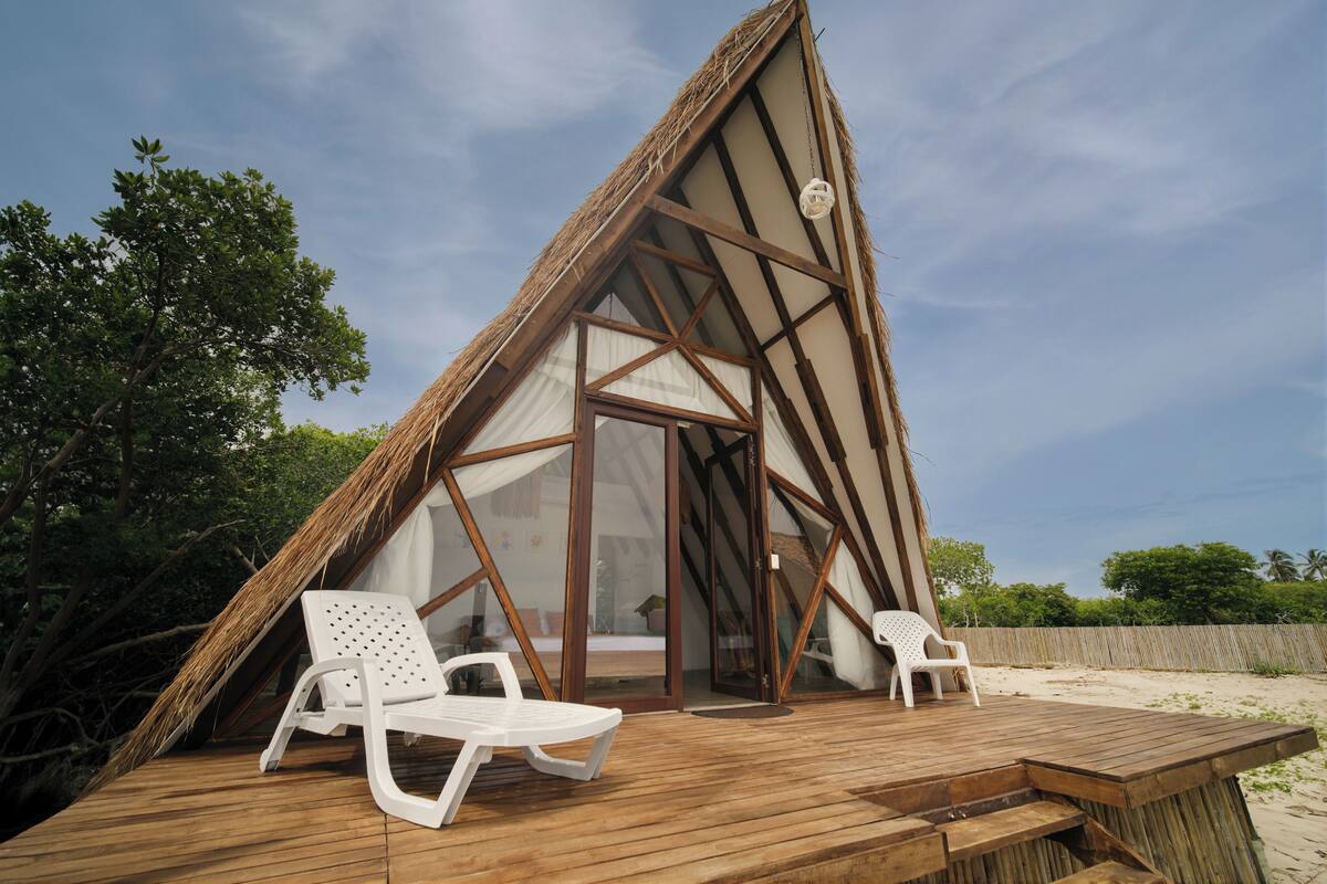 A triangular wooden structure with a glass door and two white plastic chairs on a wooden deck.