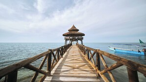 Une jetée en bois menant à une construction à toit de chaume, construite sur l’eau.