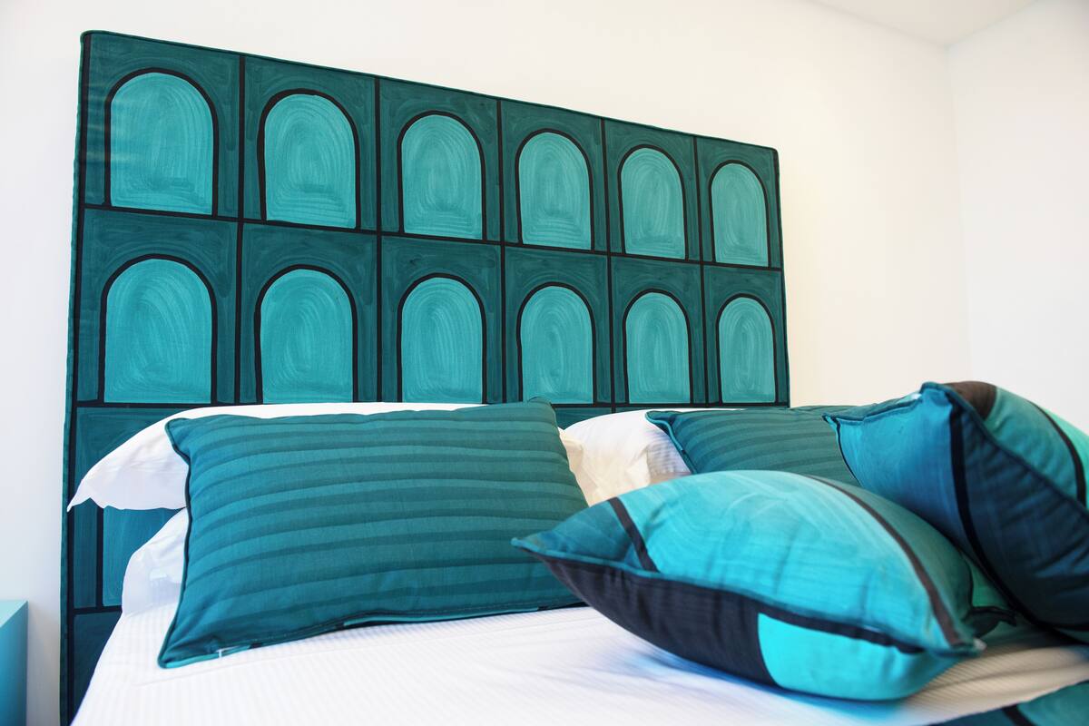 Una cama con muchos almohadones y un cabecero con diseño geométrico.
