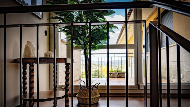 Una escalera con barandilla de metal, una silla de madera, una planta en maceta y una cesta de mimbre.