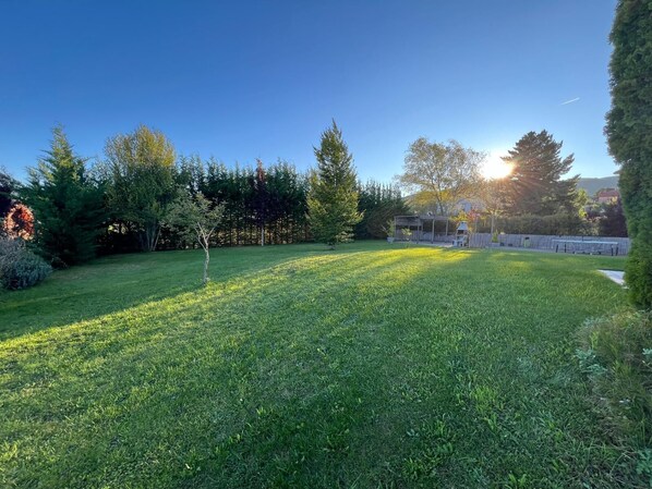 A well-maintained grassy backyard with a wooden deck and a barbecue area.