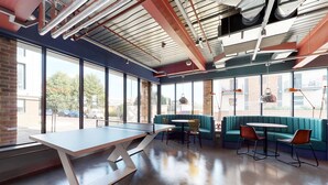 A modern indoor space with a ping pong table, seating area, and large windows offering views of the outside. - For Students Only The Bridge in Newcastle (Newcastle-upon-Tyne)