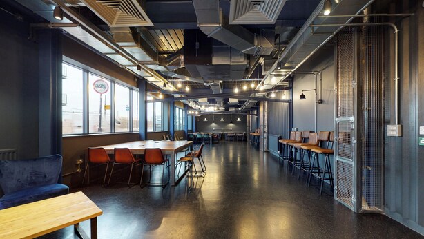 A spacious, modern lounge area with high ceilings, exposed ductwork, and a polished concrete floor. - For Students Only The Bridge in Newcastle (Newcastle-upon-Tyne)
