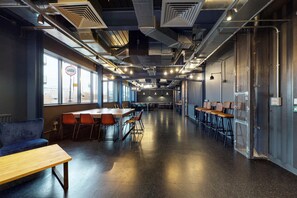Un salón amplio y moderno, con techos altos, conductos expuestos y piso de concreto pulido.