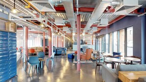 A modern office space with a central seating area, multiple tables, and chairs. - For Students Only The Bridge in Newcastle (Newcastle-upon-Tyne)