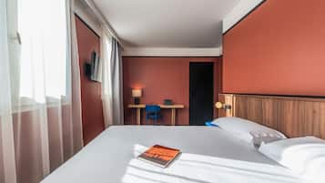 A hotel room with a bed, a desk, a chair, and a TV.