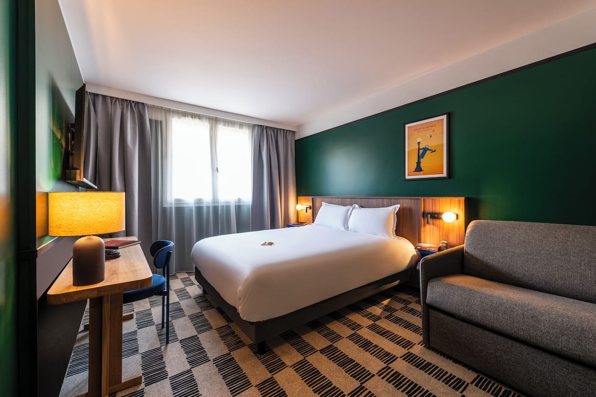 Une chambre d’hôtel avec un grand lit, un bureau avec une lampe, un canapé et un tableau au mur.
