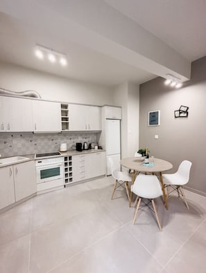 A modern kitchen with white cabinetry, a dining table with four chairs, and a refrigerator.