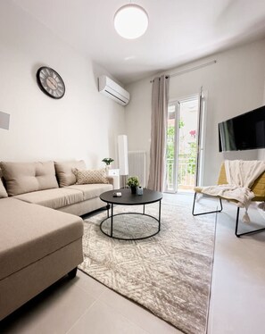 A modern living room with a sofa, a coffee table, a TV, and a window with curtains.