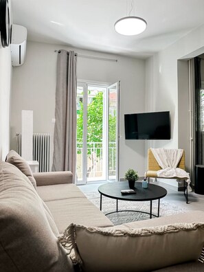 Ett modernt vardagsrum med en soffa, ett soffbord, en tv och en skjutdörr i glas som leder ut till en balkong.