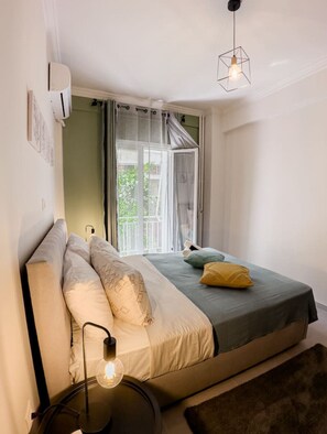 A bedroom with a bed, pillows, a bedside lamp, and a window with curtains. - Metro Chic Renovated Studio (Athina)