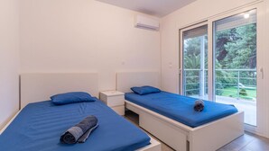 A bedroom with two beds, a small bedside table, and a sliding glass door leading to a balcony.