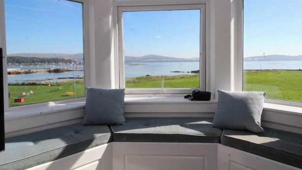 A room with a large window seat overlooking a lake and distant mountains. - Fairview (Isle of Cumbrae)