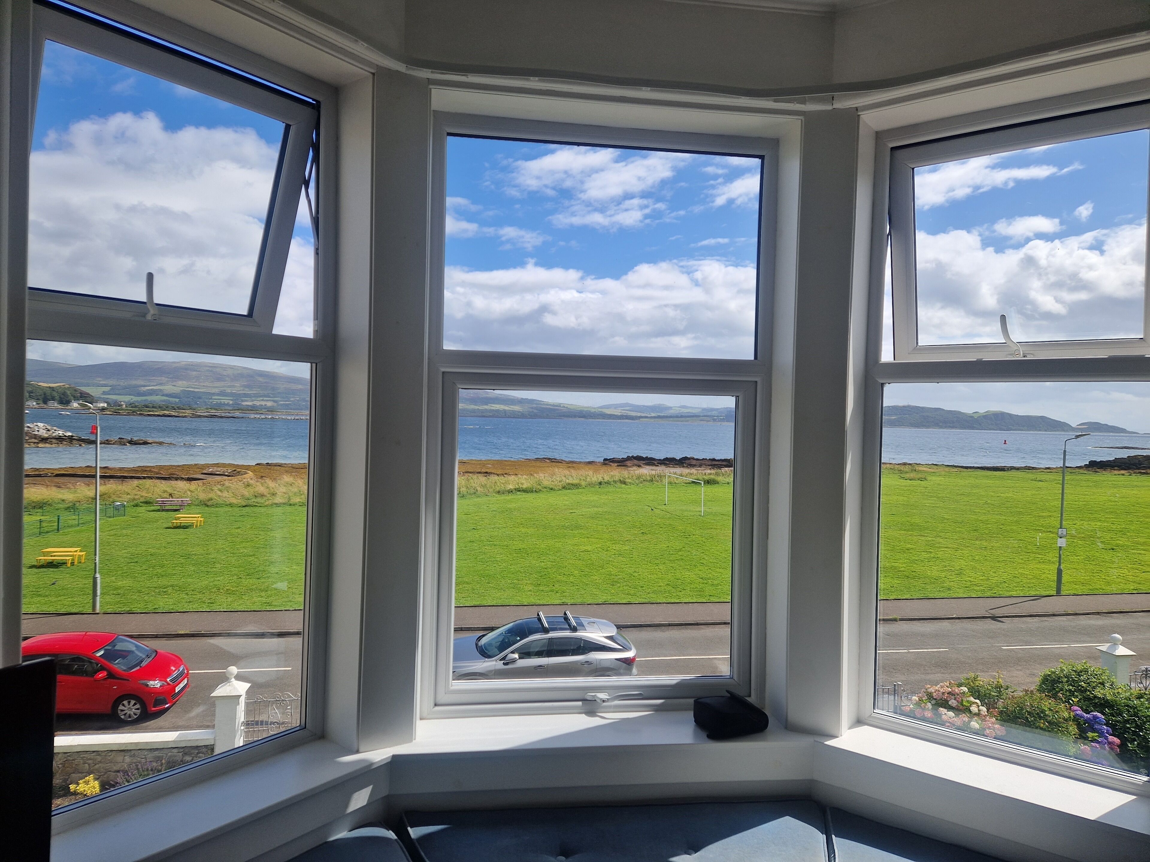 A bay window with a view of a grassy field, a body of water, and distant mountains.