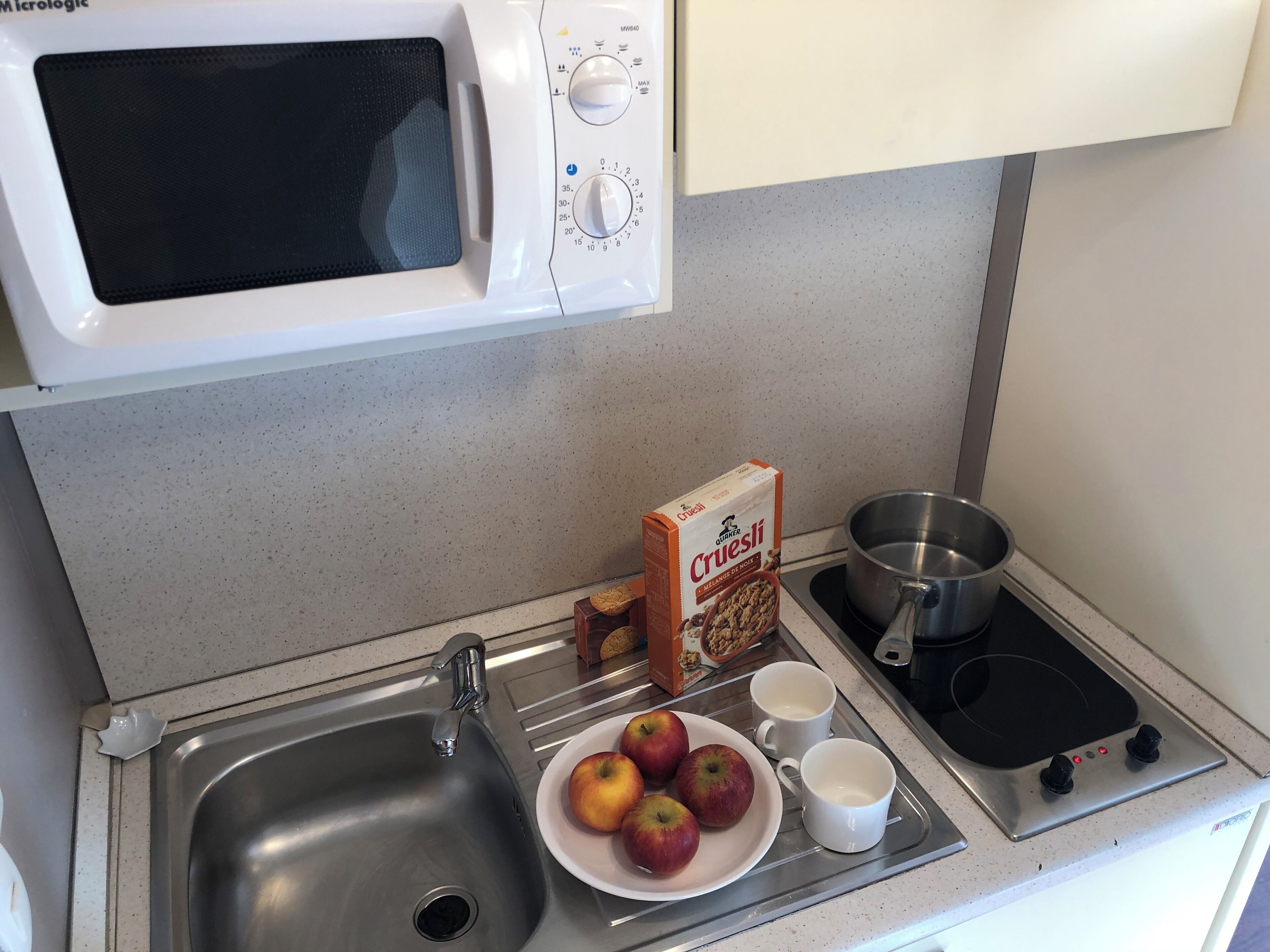 A kitchen with a microwave, sink, stove, and a plate of apples.