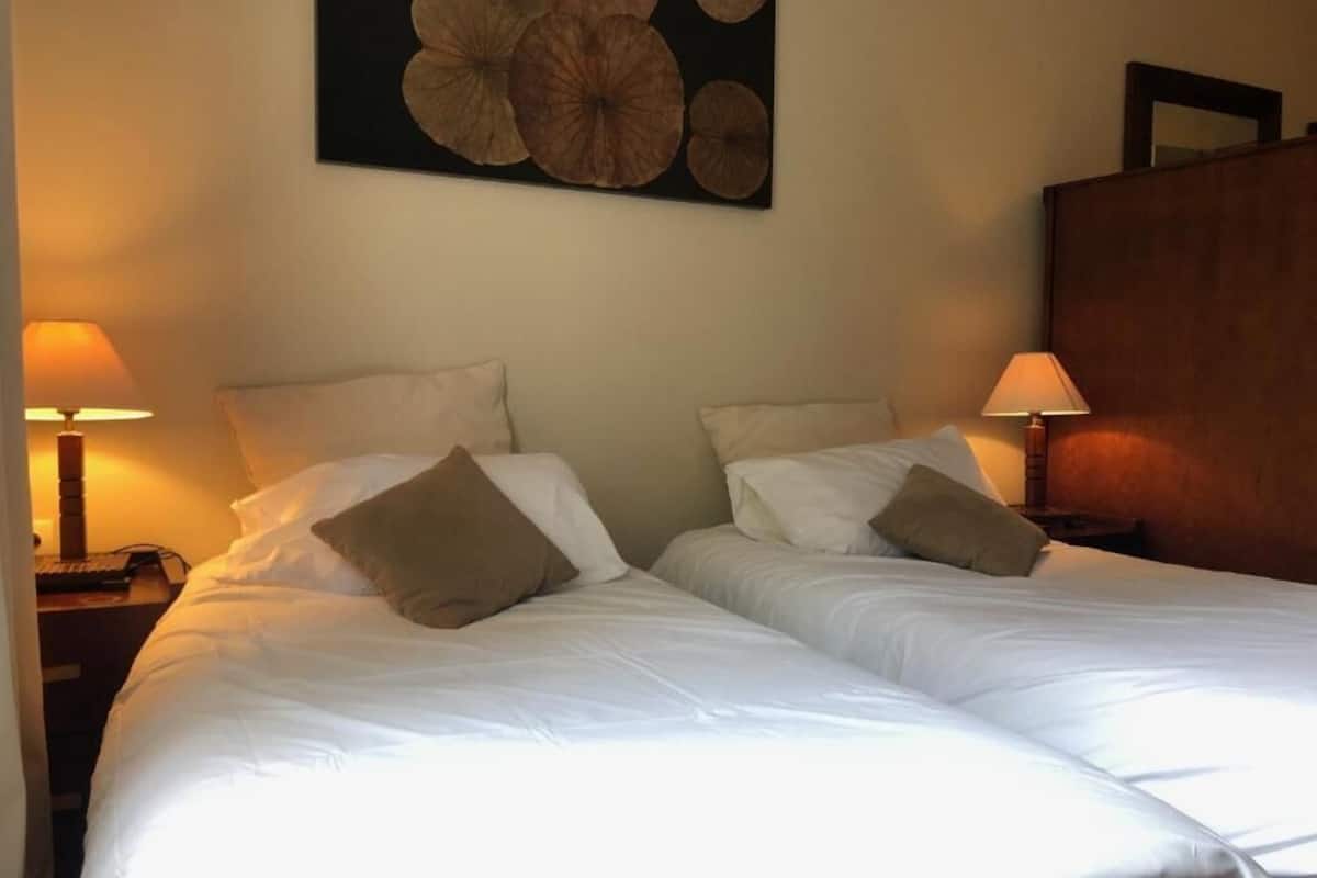 A double bed with white linens and two pillows, flanked by nightstands with lamps, in a room with a large abstract painting on the wall.