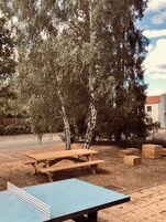 Un área de picnic con una mesa y bancos, rodeada de árboles y un edificio al fondo.