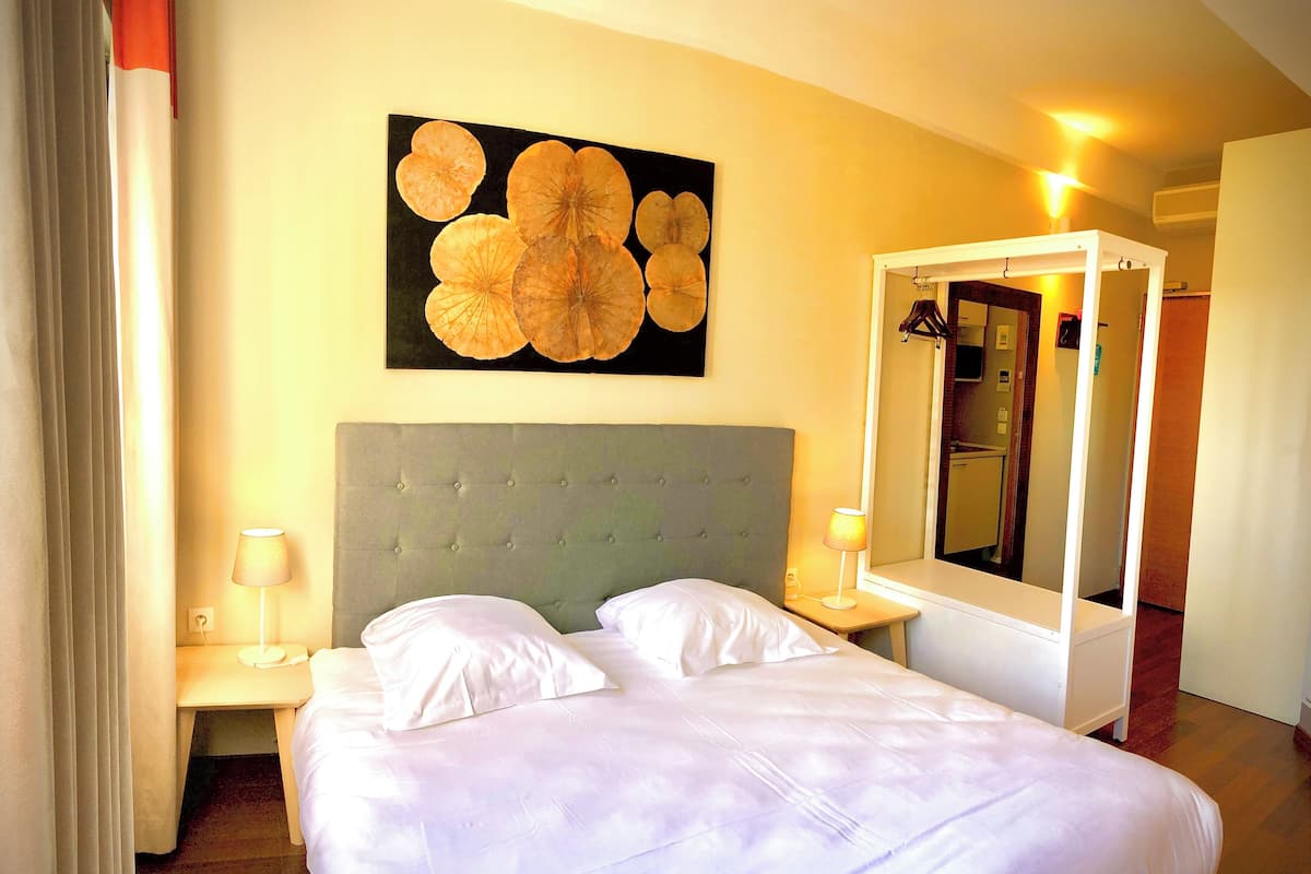 A hotel room with a bed, two bedside tables, a large mirror, and a wall art piece.